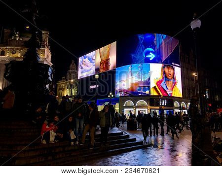 LONDON - APRIL 4, 2018: Tourists lit up at night by bright advertising illumination screens in Piccadilly Circus, Westminster, London, UK.