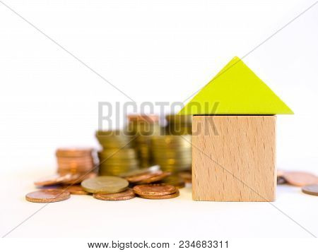 Coins And Blocks - Close Up Small Blocks House On Blurred A Pile Of Coins. The Concept Of Purchase O