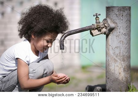 African American child drinking water from tap outdoors. Water scarcity concept