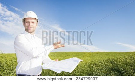 Geodesist With Drawings On Ground For Building Building. Builder In White Helmet And Project Documen