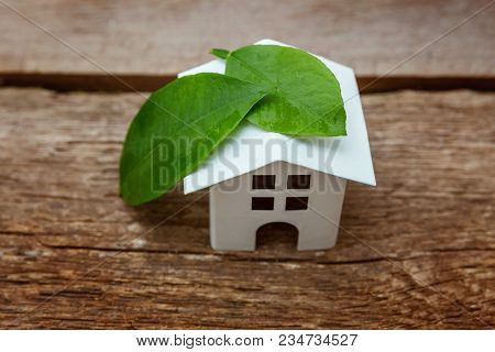 Miniature White Toy Model House With Green Leaves On Wooden Backgdrop. Eco Village, Abstract Environ
