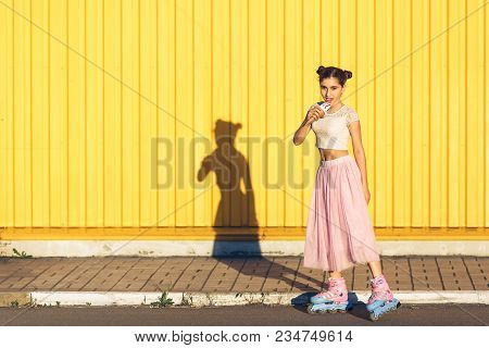 Young Girl In Summer Rollerblading And Eating Ice Cream On Yellow Wall Background. Concept Summer En