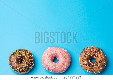 Three Colorful Donuts, Blue Background. Copy Space