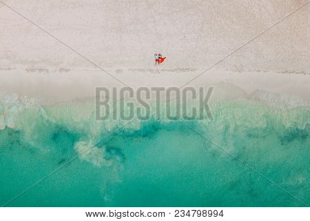 Drone Photo. The Couple Lies On The Beach. Just Ocen With Wave And White Sand