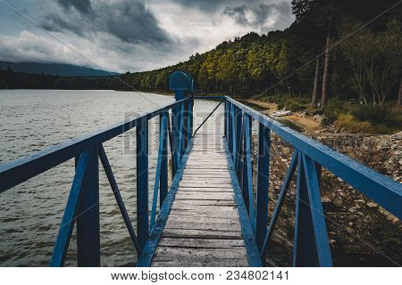 Mole (pier) On The Scandinavian Lake With Motorboat On Side And Misty Hills. Blue Wooden Bridge In F