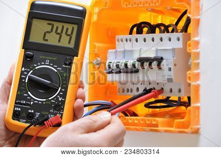 Electrician Technician Working On A Residential Electrical Panel, Measures The Voltage On The Termin
