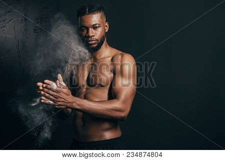 Young Bare-chested African American Sportsman Applying Talcum Powder And Looking At Camera On Black