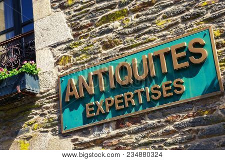 Closeup Signboard Of Antiquites Expertises Written In Golden On Green Banner Against Wooden Brick Wa