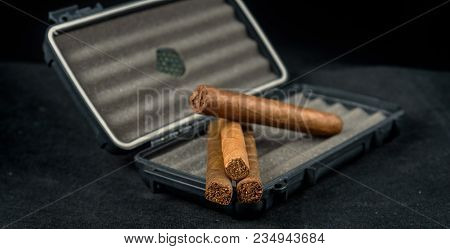 Cigars On Top Of A Black Travel Humidor. Rich Smelling And Textures Of Tobacco Leaves