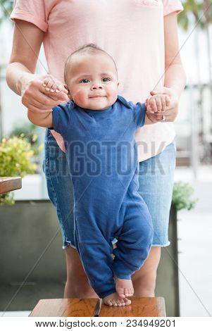 Adorable bi-racial baby boy learning to walk with the help of his mother. This happy cute child is learning how to move on his own for the first time. His first steps forward