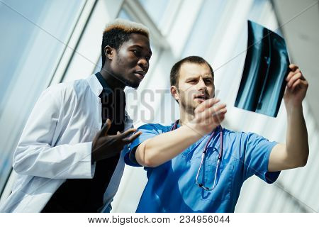 Two Doctors Holding And Analysing An Xray In A Bright Modern Office Office. Multi Ethnic Doctors Dis