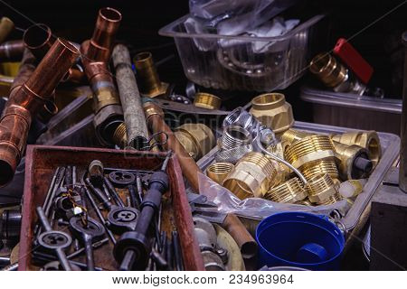 Copper And Steel Pipes, Various Connectors, Tools On A Plumber Table In A Workshop. Close Up.