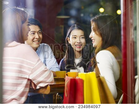 Four Happy Young Asian Adults Male And Female Relaxing Chatting Talking In Coffee Shop After Shoppin