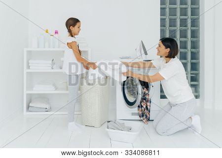 Happy Mother Loads Clothes In Washing Machine, Little Girl Helps, Gives White Linen From Basket, Do 