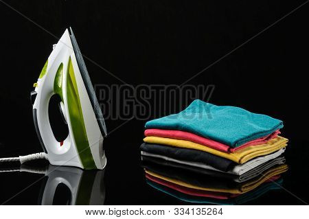 Electrical Green And White Hand Iron And Stack Of T-shirts On The Black Mirror Background With Copy 
