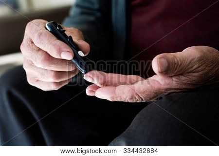 closeup of a caucasian old man about to measure his blood glucose level in a glucose meter by pricking his finger with a fingerstick