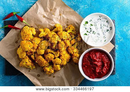 Baked Cauliflower With Tomato And Sour Cream Sauce On Parchment Paper On Blue Background. Vegetarian