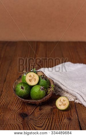 Green Feijoa In A Coconut Shell Hulf On A Wooden Background. Ripe Tropical Fruits, Raw Vegan Food.vi