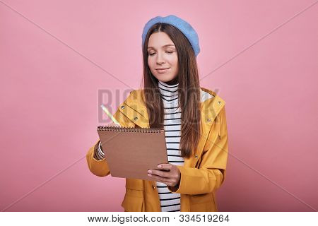Cute Student With Beaytiful Smile In A Yellow Jacket, A Striped Sweater And A Blue Headdress Is Stan
