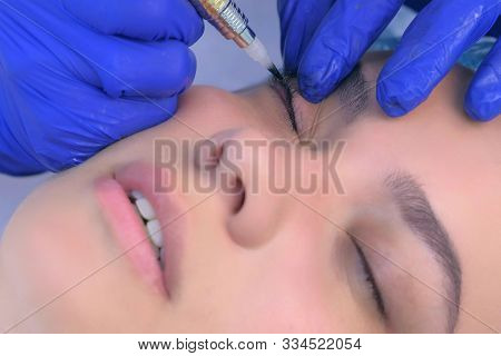 Premanent Eyeliner On Eyelids For Young Woman In Beauty Clinic, Closeup Face. Cosmetologist Making B