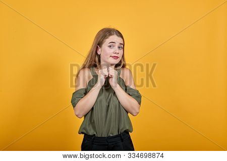 Pretty Young Caucasian Lady Keeping Fists On Chest With Over Orange Background. Looks Happy, Funny W