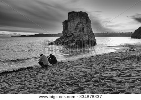Two Men Surfing With Their Mobile Phones On A Beach During A Beautiful Sunset At St. Austell, Cornwa