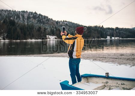 In The Middle Of Nature With A Big Lake And Snowy Mountain And Forest Young Man With Orange Jacket T