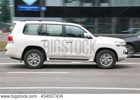 Toyota Land Cruiser 200 Side View. Big Suv White Color Driving Against A Background Of Glass Buildin