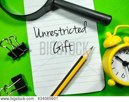 Business Concept.text Unrestricted Gift Writing On Notepaper With Magnifying Glass,paper Clips,clock