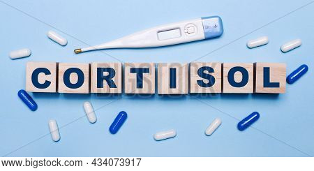 On A Light Blue Background, An Electronic Thermometer, White And Blue Pills And Wooden Cubes With Th