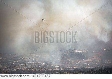 Helicopter With Water Bucket Flying In Heavy Smoke Over Rural Area, Fighting Wildfire