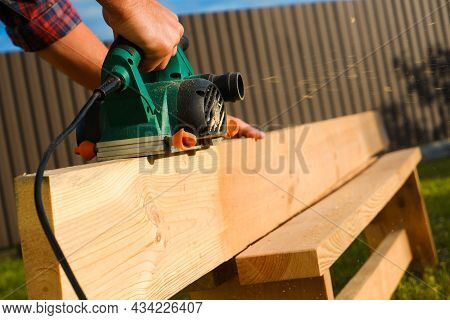 A Carpenter Planes A Wooden Board With An Electric Plane. Planing Wooden Plank With A Electric Plane