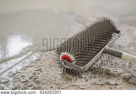 Plasterer During Floor Covering Works With Self-levelling Cement Mortar, Uses A Needle Roller