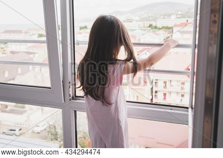 One Child Is Dangerously Standing At An Open Window. Children And Open Windows. A Girl In Night Paja