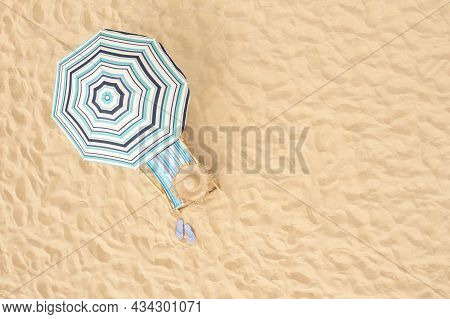 Striped Beach Umbrella Near Sunbed With Vacationist's Stuff On Sandy Coast, Aerial View. Space For T