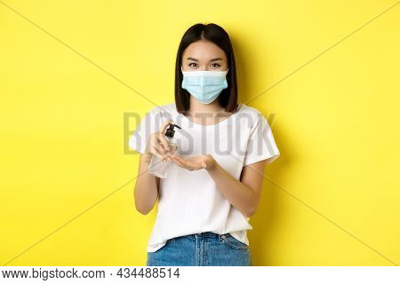 Covid, Health Care And Pandemic Concept. Cute Asian Woman In Medical Mask Using Hand Sanitizer To Di