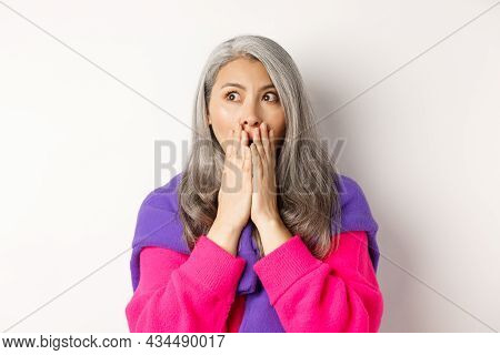 Close-up Of Shocked Asian Middle-aged Woman With Grey Hair, Gasping And Covering Mouth Startled, Loo