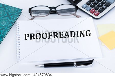 Text Proofreading On A White Notebook On The Table Next To The Calculator, Glasses, Pen