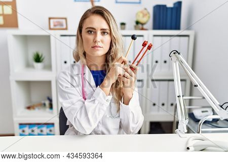 Young beautiful doctor woman holding diapason instrument relaxed with serious expression on face. simple and natural looking at the camera. 