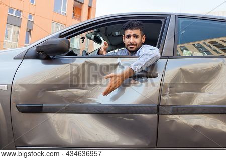 Portrait Of Confused Handsome Bearded Man Wearing Blue Shirt Sitting Behind The Wheel Of Dented Car 
