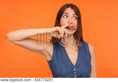 Funny Comical Brunette Woman In Denim Dress Picking Nose And Showing Tongue With Humorous Stupid Exp