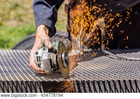 An Image If Hands Of A Female Welder Holding An Electronic Disc Grinder, Welding A Metal Rod, Fire S