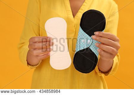 Young Woman With Reusable Menstrual Pad And Pantyliner On Yellow Background, Closeup