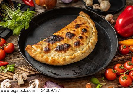 Pizza Calzone On A Black Plate With Vegetables