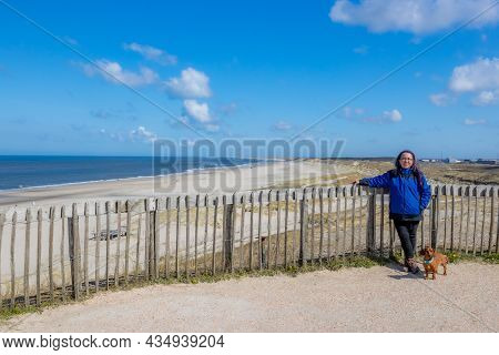 Female Tourist With Her Brown Short Haired Dachshund On The Lookout With The Beach And The Sea In Th