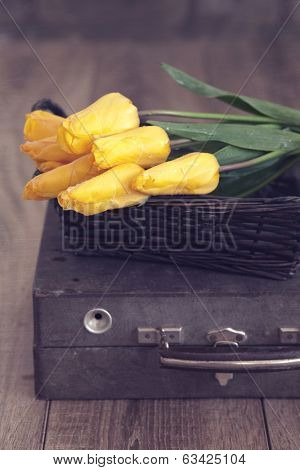 Vintage shabby chic photo of bouquet of spring tulips in a wicker basket on suitcase