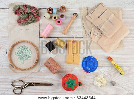 High angle shot of an assortment of sewing and embroidery tools on a rustic wooden background.