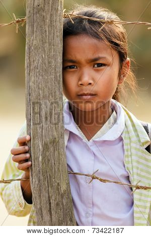 SAYABURY, LAOS, FEBRUARY 16, 2012: Laotian little girl posing near a fence pole in the schoolyard during the Elefantasia festival in Sayaboury, Laos