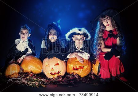 Cheerful children in halloween costumes posing with pumpkin over dark background.