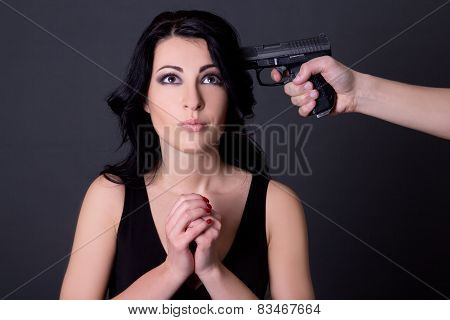 Young Beautiful Woman Hostage And Male Hand With Gun Over Grey
